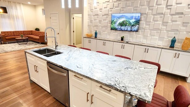 Una cocina moderna con encimera de mármol, armarios blancos y lavavajillas integrado.