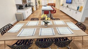 Una cocina moderna con armarios blancos, una isla central y un comedor con una mesa larga y sillas.