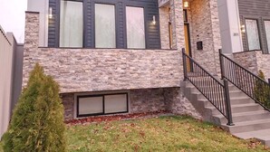 Una casa moderna de dos pisos con fachada de piedra, ventanas amplias y una escalera visible que lleva a la entrada.