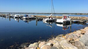 A marina with boats docked, calm water, and a rocky shoreline.