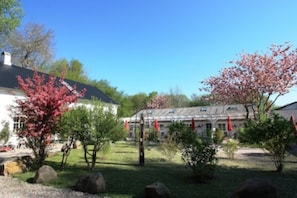 Une cour avec un bâtiment blanc, une serre et des cerisiers en fleurs.