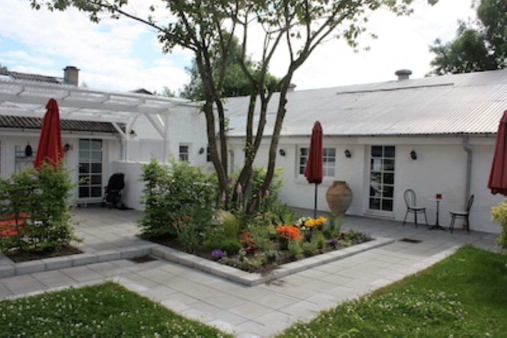 Une cour avec un bâtiment blanc, des parasols rouges et une variété de plantes.