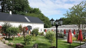 A white building with a dark roof, surrounded by a well-maintained garden with rocks, shrubs, and a pathway.