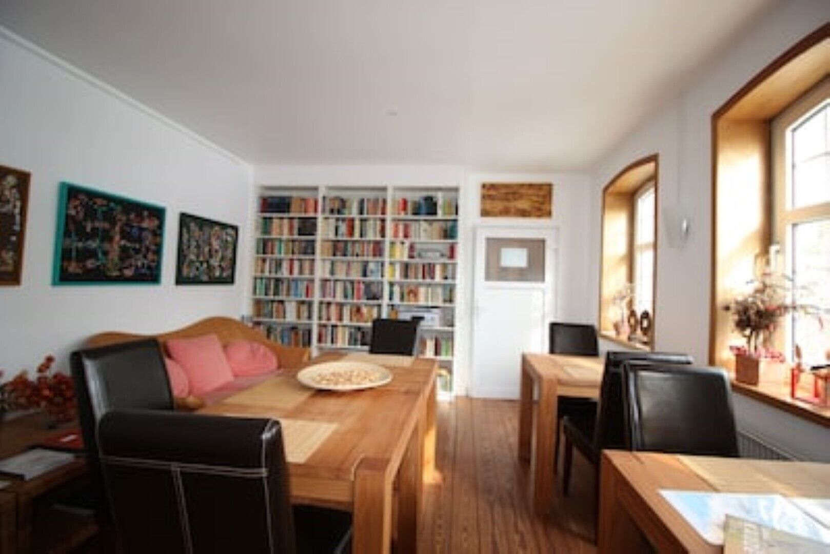 A cozy living room with a wooden coffee table, a sofa with a pink cushion, and a bookshelf filled with books.