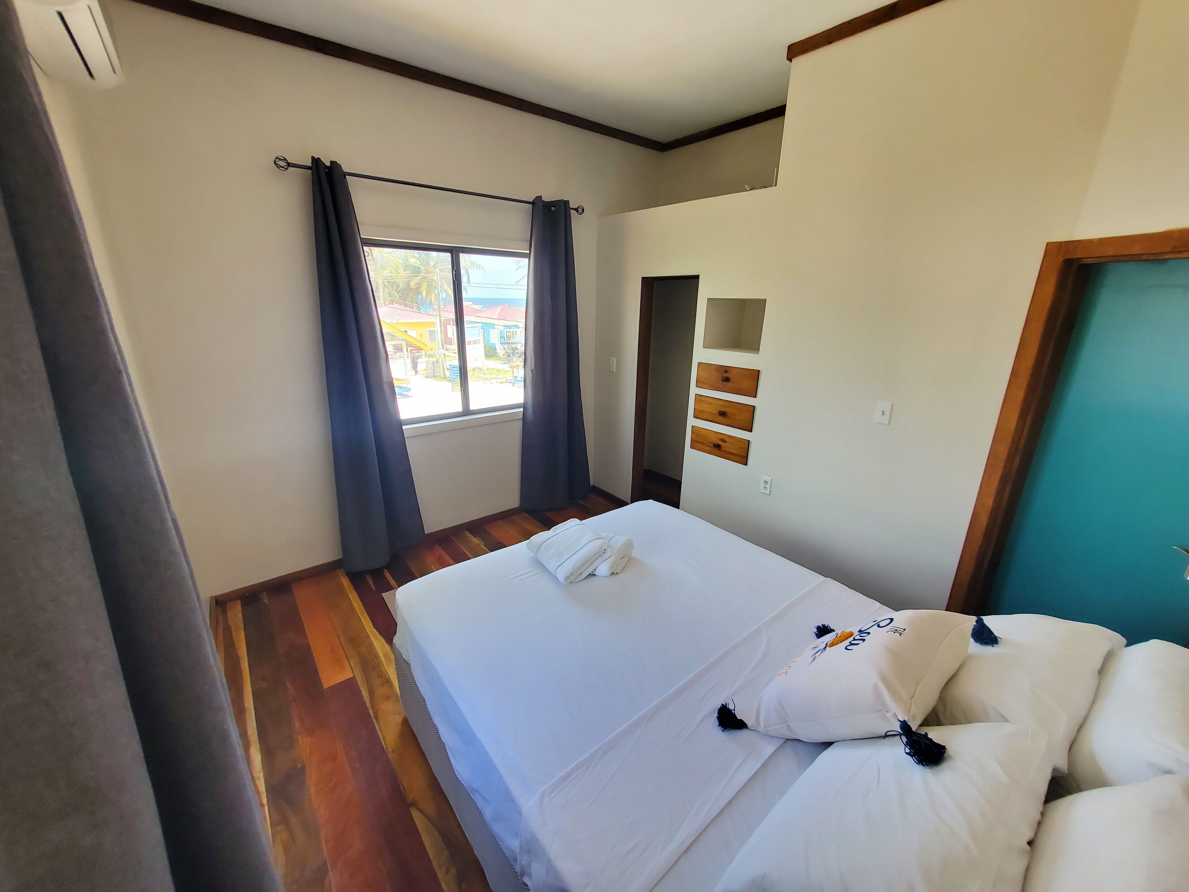 A hotel room with a bed, a window with curtains, a wooden floor, and a door with a mirror and wooden panels.