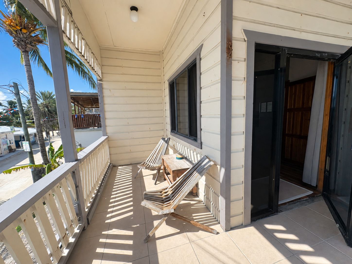 A covered outdoor area with a wooden bench, a table with a stack of boards, and a door leading to an interior space.