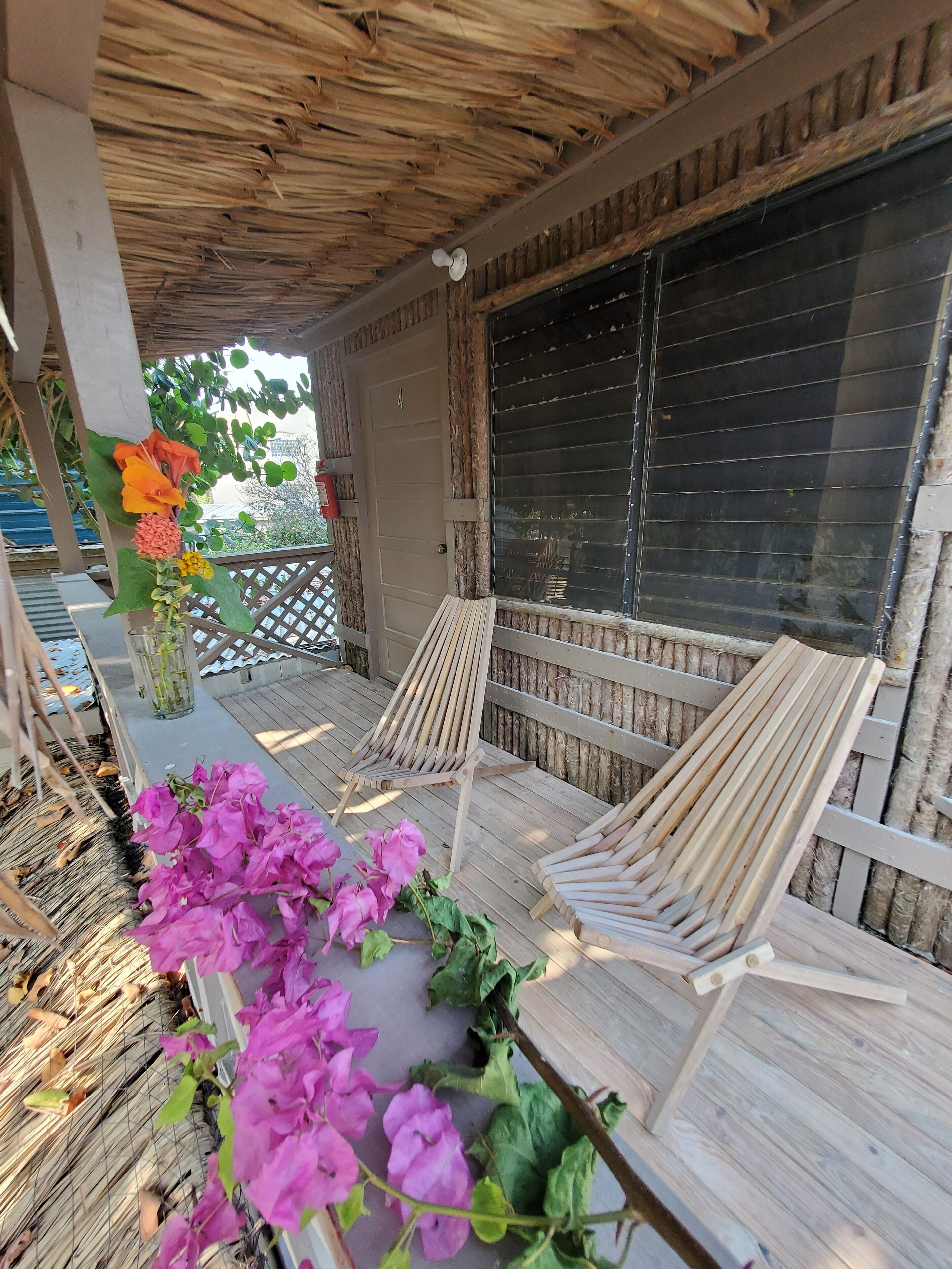 A wooden deck with two lounge chairs, a glass door, and a thatched roof.
