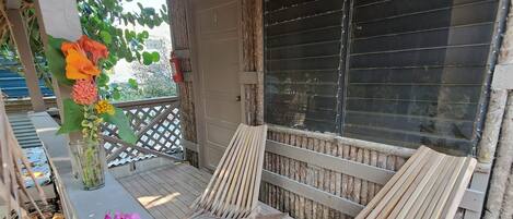 A wooden deck with two lounge chairs, a glass door, and a thatched roof.
