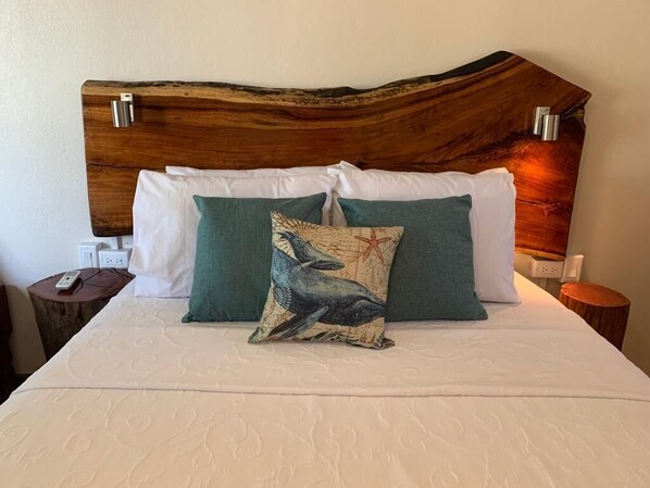 Uma cama com cabeceira de madeira, almofadas brancas e azul-turquesa, e uma almofada decorativa com desenho de pássaro.