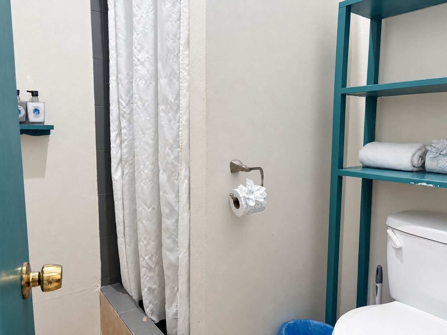 A bathroom with a toilet, a shelf with toiletries, and a shower curtain.