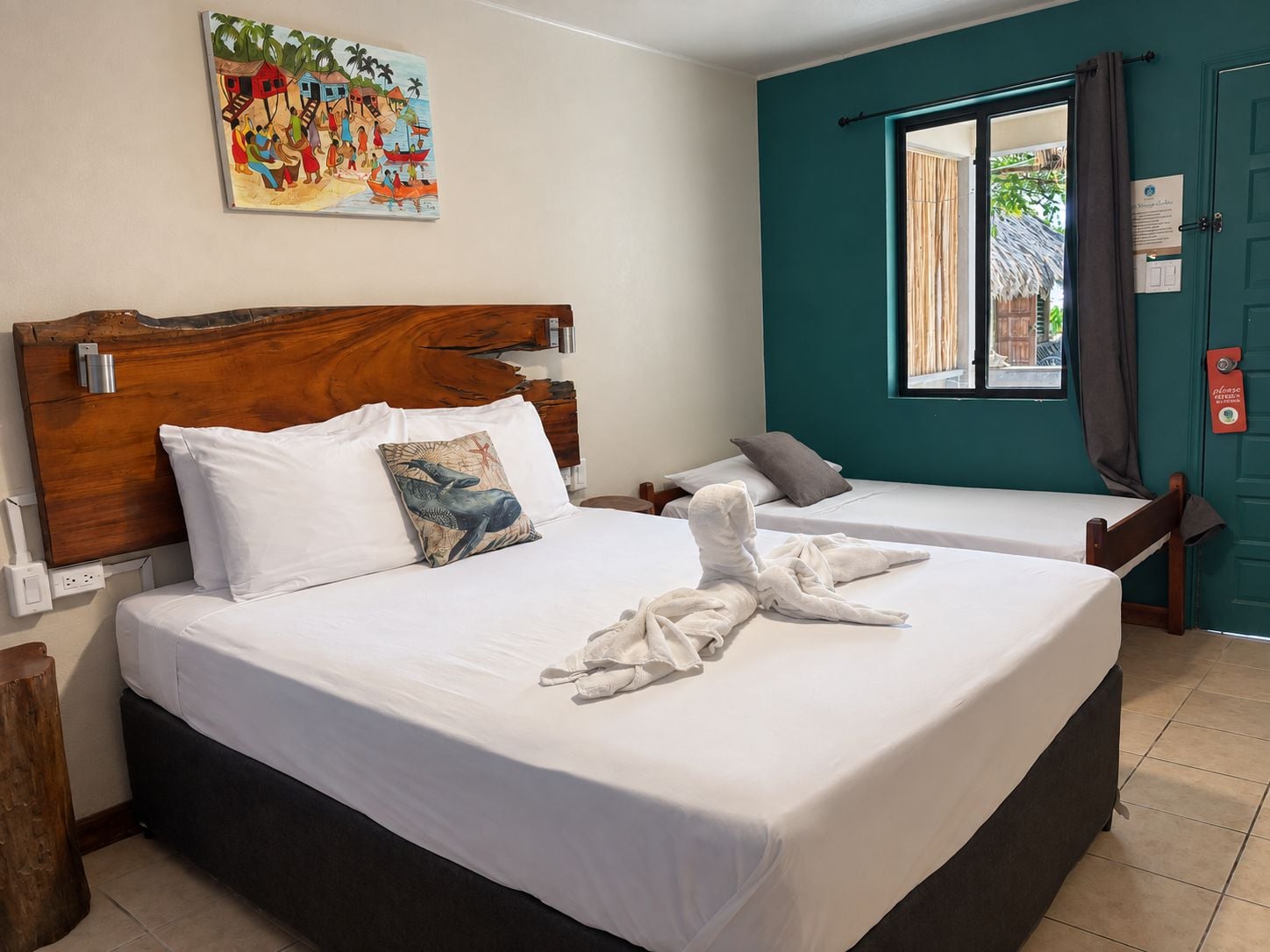 Habitación de hotel con dos camas, cabecero de madera, un cuadro en la pared y una ventana con cortinas.