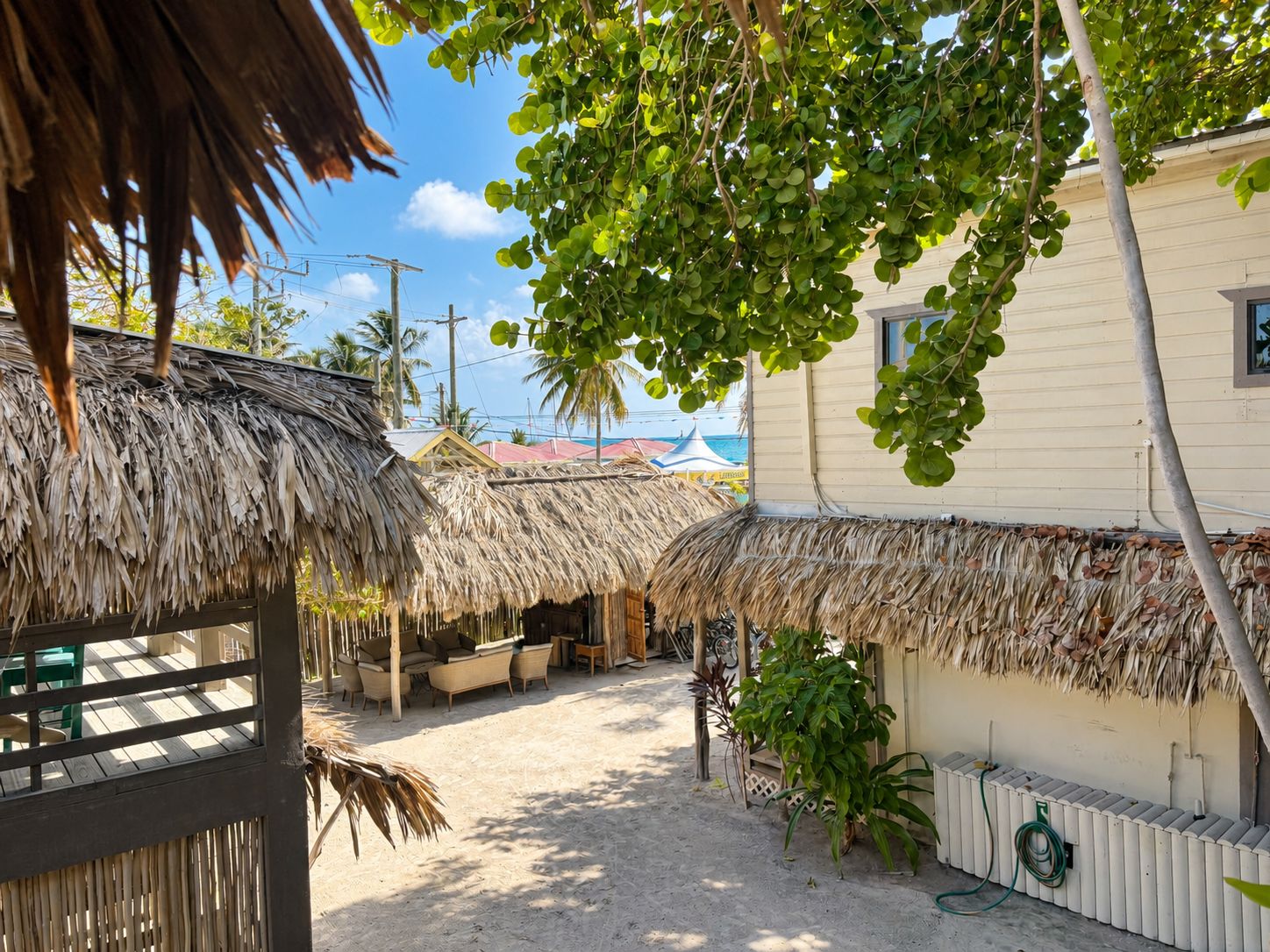 A beachside area with thatched-roof structures, outdoor seating, and a white building.