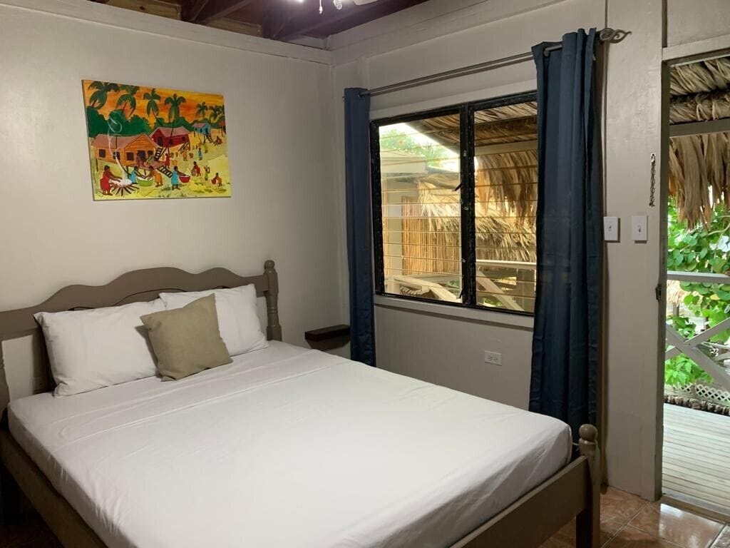 Une chambre à coucher avec un lit, une fenêtre avec des rideaux, un tableau au mur et une vue sur l’extérieur.