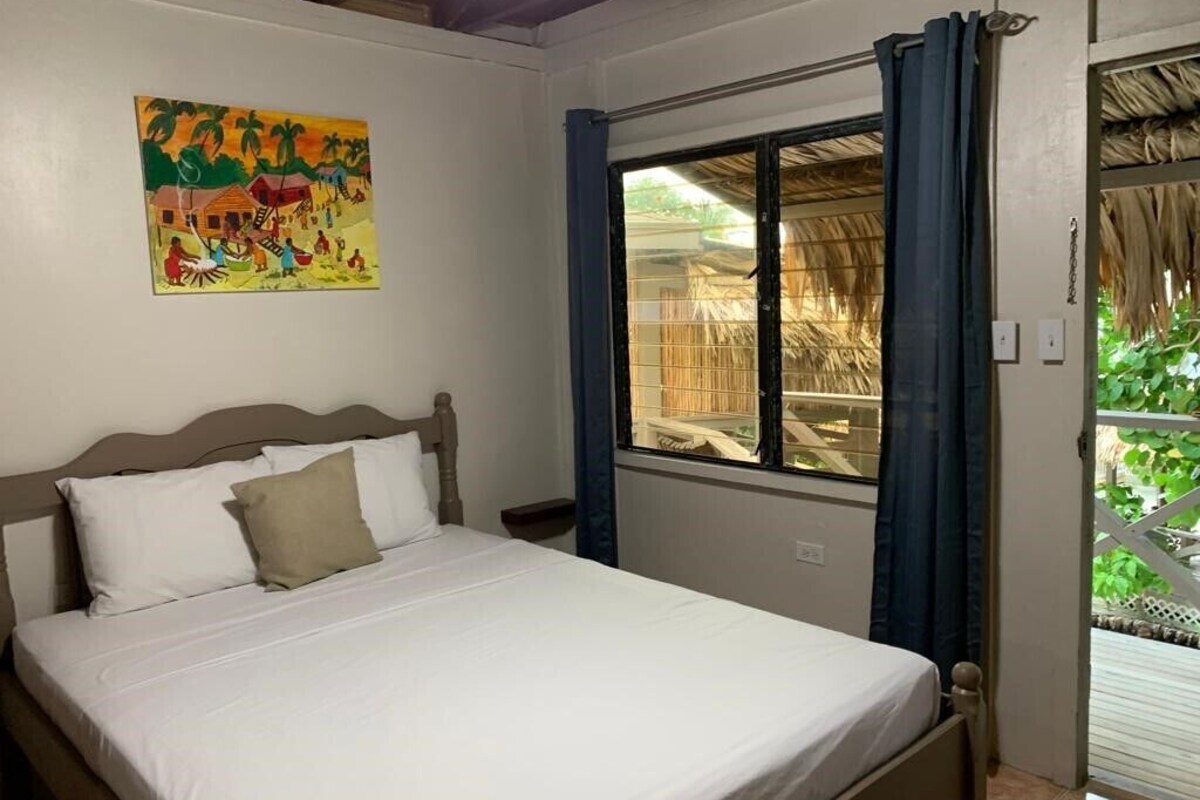 Une chambre à coucher avec un lit, une fenêtre avec des rideaux, un tableau au mur et une vue sur l’extérieur.