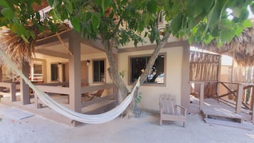 Eine Strandhütte mit einer Hängematte, Holzstühlen und einem Reetdach.