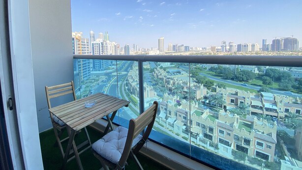 A balcony with a table and chairs, overlooking a cityscape with modern buildings and a highway. - Lux BnB Elite Residences I Golf Course Views (Dubai)