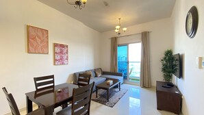 A modern living room with a dining area, a sofa, a TV, and a balcony with a view. - Lux BnB Elite Residences I Golf Course Views (Dubai)