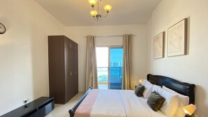 A bedroom with a bed, nightstands, a wardrobe, a chandelier, and a view of the city through a balcony. - Lux BnB Elite Residences I Golf Course Views (Dubai)