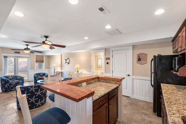 A kitchen with a central island, wooden cabinets, and a refrigerator. - Another Day In Paradise: 4-Min Walk to the Beach! (Kill Devil Hills)