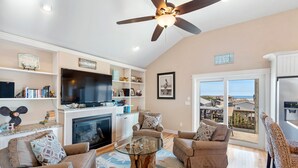 A spacious living room with a fireplace, comfortable seating, a flat-screen TV, and a balcony with a view. - Another Day In Paradise: 4-Min Walk to the Beach! (Kill Devil Hills)