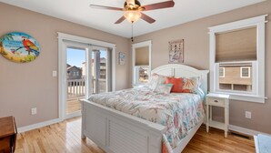 A bedroom with a bed, ceiling fan, wooden floor, and a view of the outside. - Another Day In Paradise: 4-Min Walk to the Beach! (Kill Devil Hills)