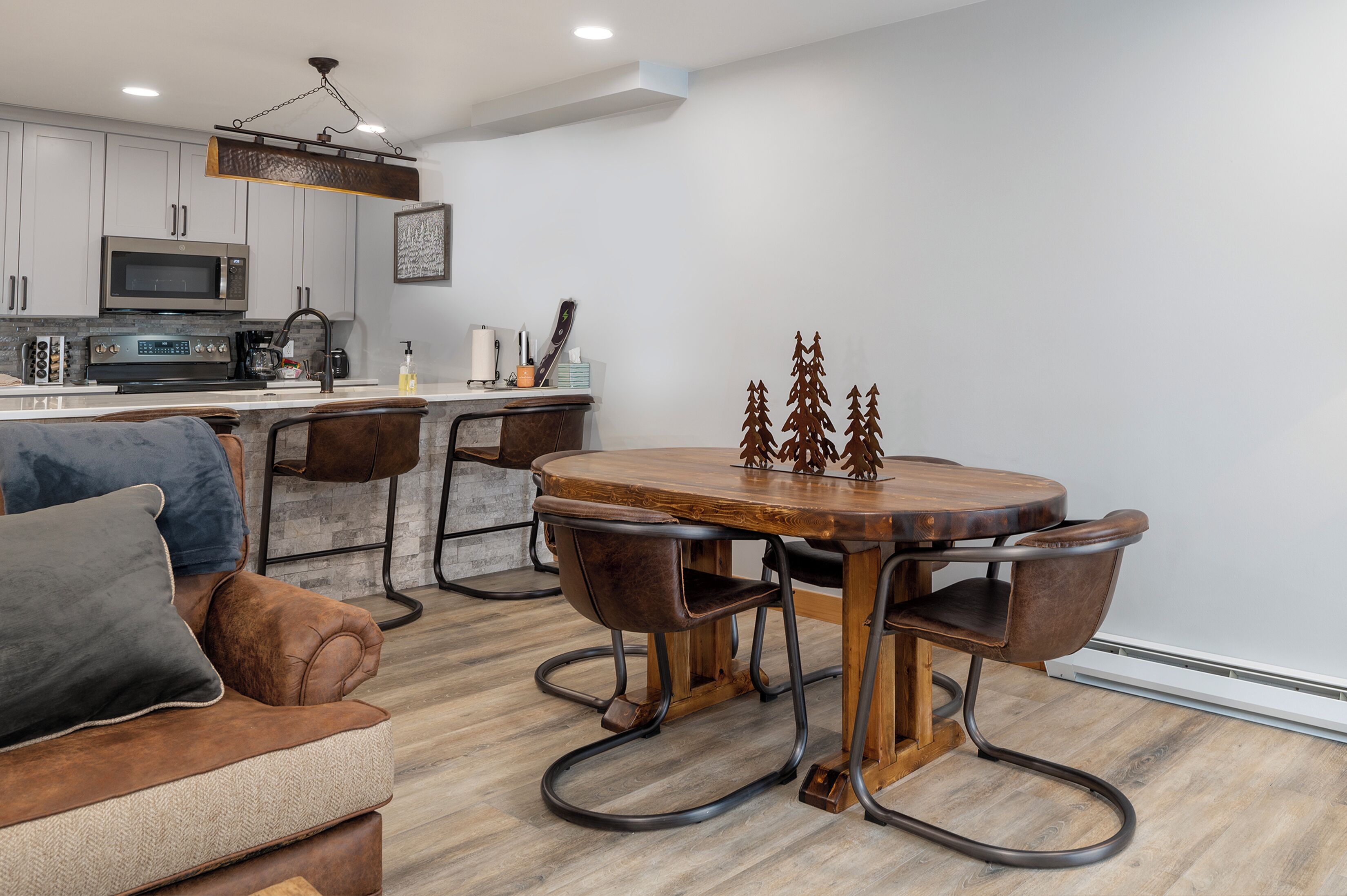 A modern kitchen with white cabinets, a microwave, and a stove. There is a dining table with chairs and a decorative tree sculpture.