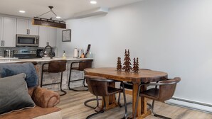 Una cocina moderna con armarios blancos, un microondas y una estufa. Hay una mesa de comedor con sillas y una escultura decorativa de un árbol.