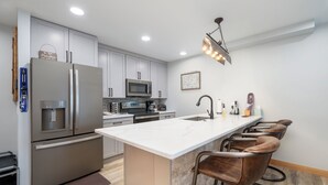 Una cocina moderna con electrodomésticos de acero inoxidable, una isla de mármol y taburetes de bar.