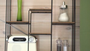 A wooden wall with a black metal shelf unit containing a vintage radio, a green vase, and two glass containers. - Tiny house in unspoiled nature on Lake Plau (Stuer)