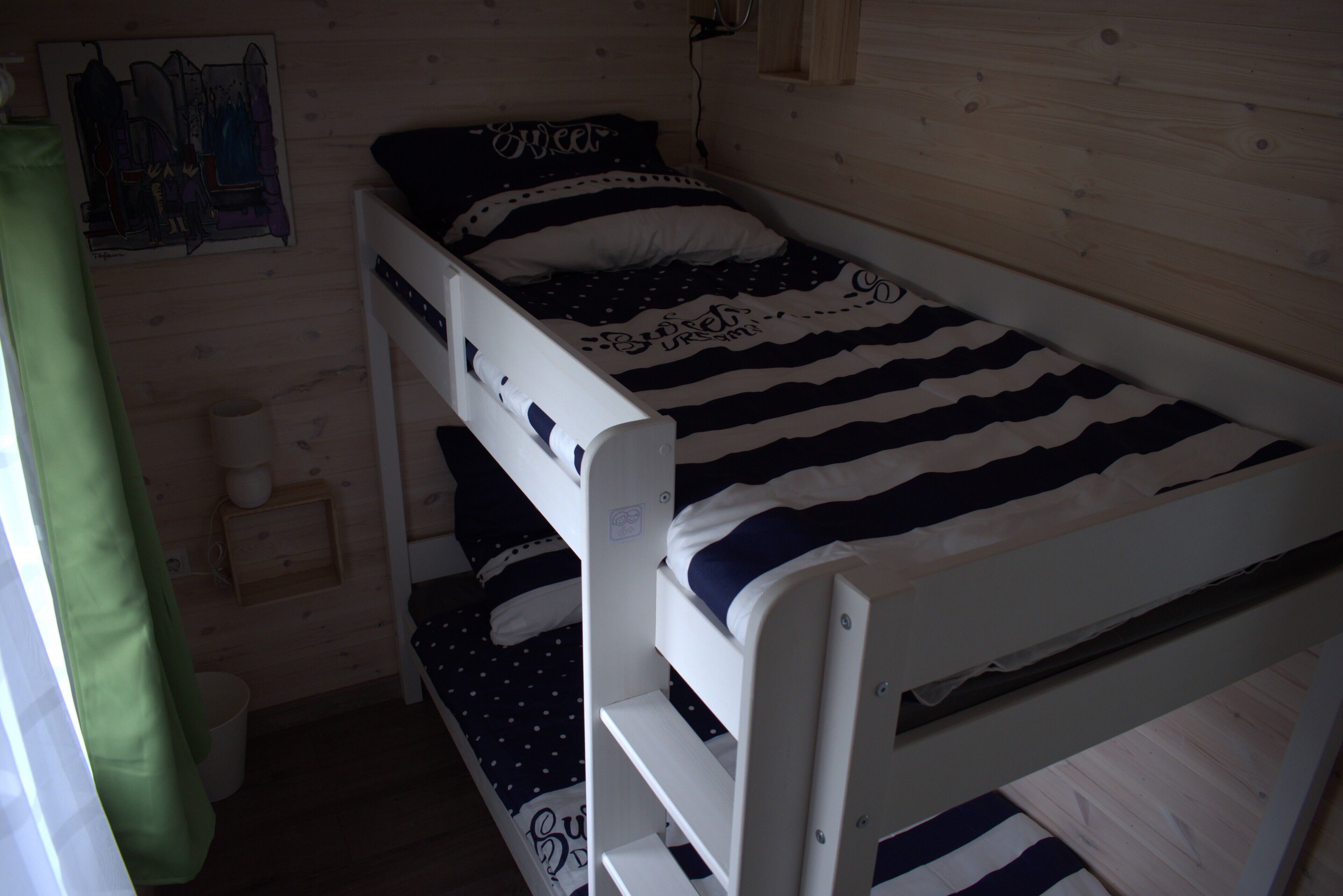 A bunk bed room with a striped bedspread, a green curtain, and a small wooden shelf.