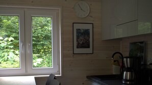 A kitchen with wooden walls, a window, a sink, a stove, and a chair. - Tiny house in unspoiled nature on Lake Plau (Stuer)