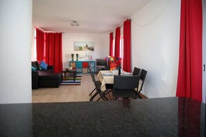Een compacte woonruimte met een eethoek, een bank, een televisie en een kleine tafel met stoelen.
