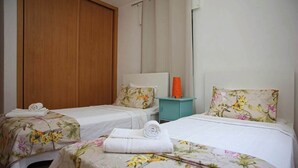 A hotel room with two single beds, each with floral bedding and a white headboard. There is a wooden wardrobe and a small teal nightstand with a lamp. - Villa Ocenano  - Stunning Ocean Views (Albufeira)