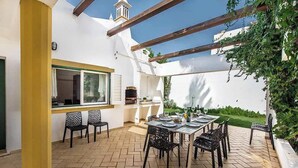 Un patio con una mesa lista para comer, rodeado de sillas y una pérgola arriba.