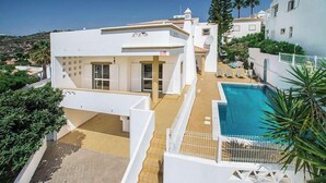 Un edificio moderno y blanco con piscina, rodeado de vegetación y otros edificios.