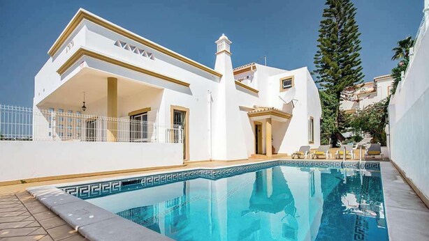 Un edificio moderno blanco con piscina, un porche cubierto y vistas del entorno.