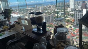 A kitchen with a coffee maker, jars, and a view of a cityscape through large windows.
