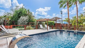 A swimming pool with a wooden deck, lounge chairs, and a pergola.
