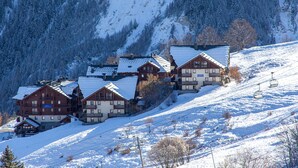 Un conjunto de edificios de madera de varios pisos, probablemente un hotel o resort, ubicados en una ladera cubierta de nieve, con un telesilla al fondo.