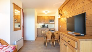 Habitación compacta con cama, mesa de comedor de madera, sillas, televisor y kitchenette con gabinetes de madera y microondas.