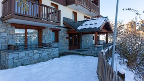 Un edificio de varios pisos con fachada de piedra, balcones de madera y una entrada cubierta de nieve.