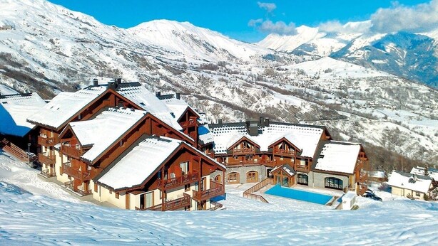 Un pueblo cubierto de nieve con chalets de madera y una piscina.