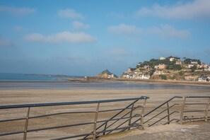 A coastal view with a beach, a staircase leading to a hilltop with buildings, and a clear sky.