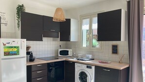 Eine kompakte Küche mit dunklen Schränken, einer Mikrowelle, einer Waschmaschine und einem Kühlschrank.