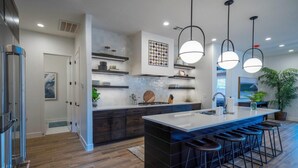 A modern kitchen with a central island, bar stools, pendant lighting, and built-in shelves. - Arcadia 63 | Sleeps 26 * Private Hot Tub * Arcades * Pool Table (Santa Clara)