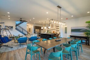 Ein modernes Wohnzimmer mit einem Holzesstisch, smaragdgrünen Stühlen, einem blauen Sofa und einer hängenden Leuchte.