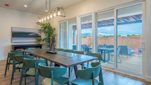 A spacious indoor dining area with a long wooden table and multiple chairs, large windows offering a view of the outdoors, and a ceiling light fixture. - Arcadia 63 | Sleeps 26 * Private Hot Tub * Arcades * Pool Table (Santa Clara)