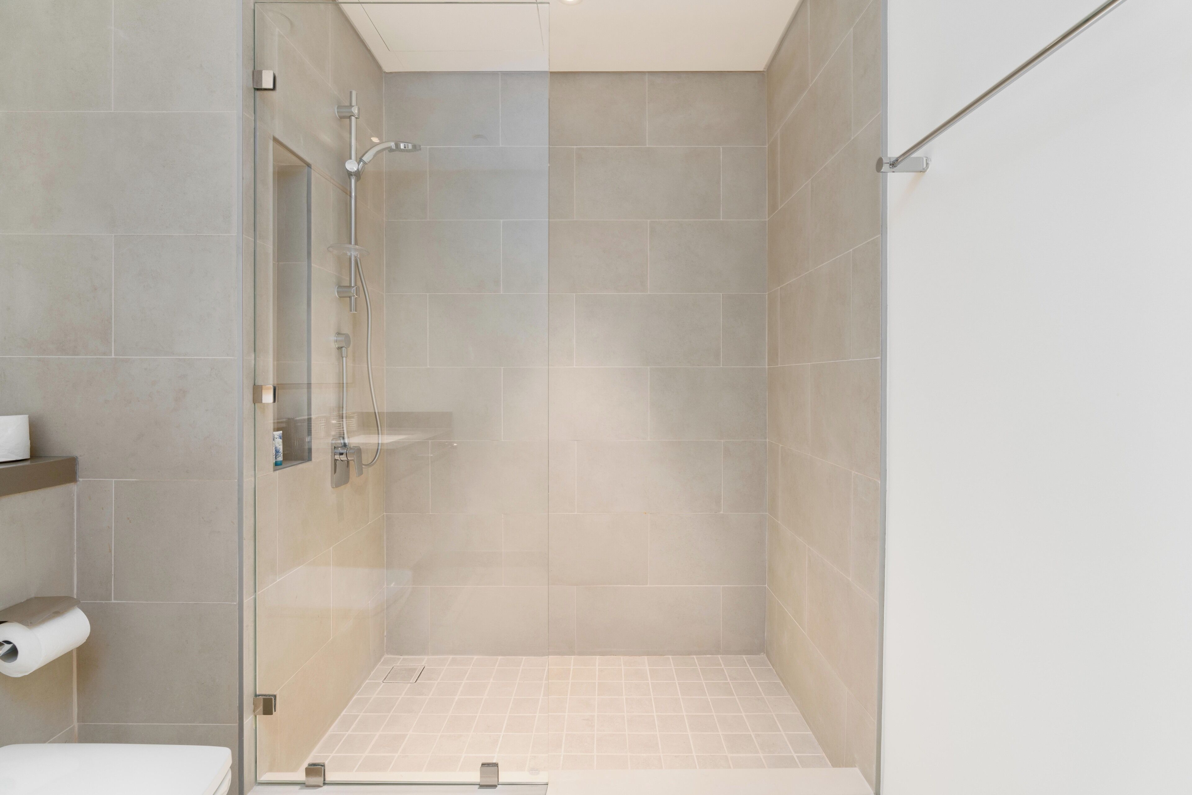 A modern bathroom with a glass-enclosed shower, tiled walls, and a toilet with a paper towel holder.