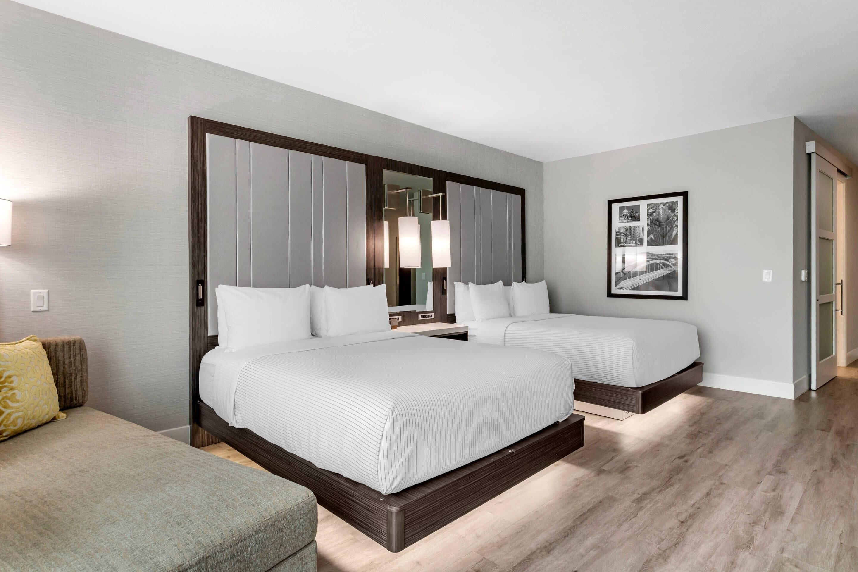 A hotel room with a large bed, a smaller bed, a sofa, a mirror, and a framed picture on the wall.