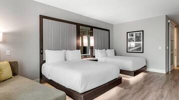 A hotel room with a large bed, a smaller bed, a sofa, a mirror, and a framed picture on the wall.